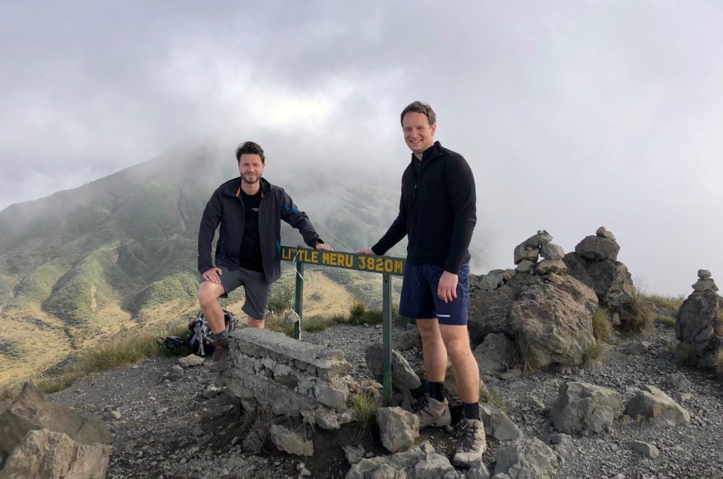 Two mountaineers stand in front of the summit sign of Little Meru